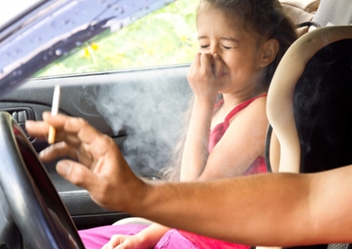 Dieťa v aute si zapcháva nos pri tom, ako jej otec fajčí.